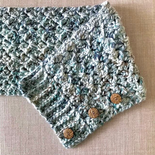 green and cream lacy crochet cowl showing placements of 3 buttons along one edge