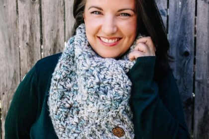 Smiling dark haired woman wearing dark green sweater, with green and cream seaglass crochet cowl with wooden buttons