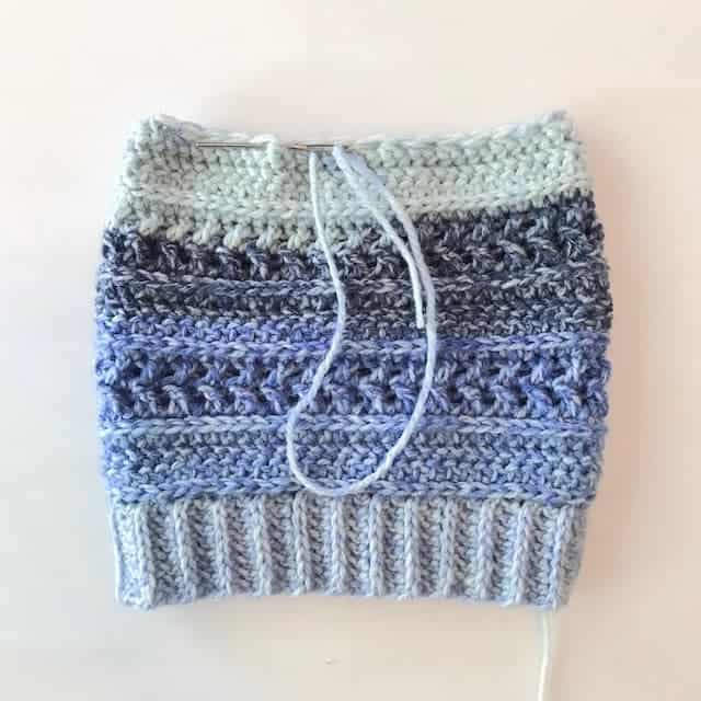 Blue crochet hat with yarn needle showing how to cinch the top closed