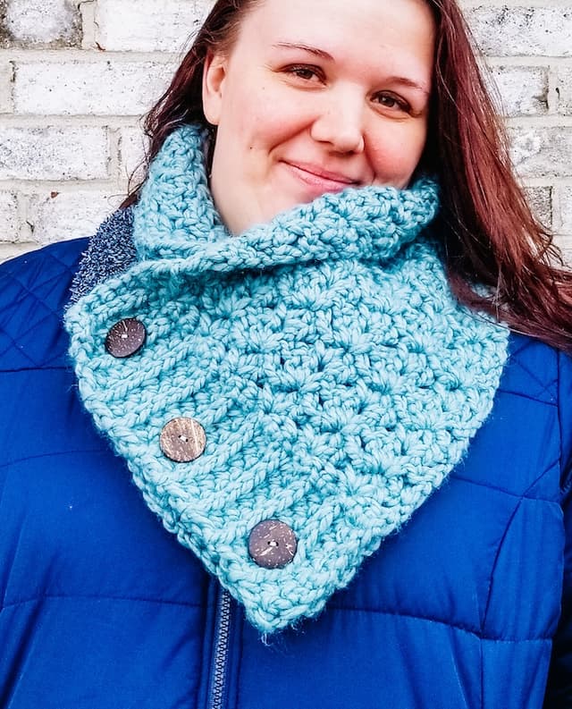 Woman wearing royal blue puffer jacket and light blue crochet cowl with the 3 buttons