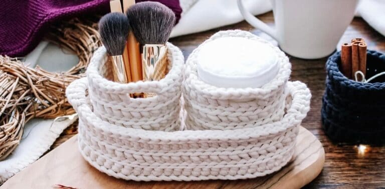 cream crochet nesting pots with two round pots containing cotton pads and makeup brushes, nestled inside a larger oval nesting basket