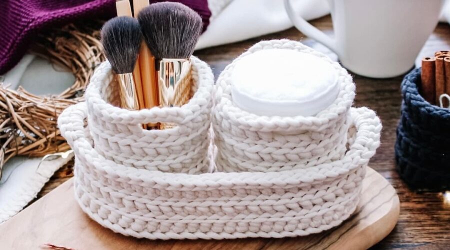 cream crochet nesting pots with two round pots containing cotton pads and makeup brushes, nestled inside a larger oval nesting basket