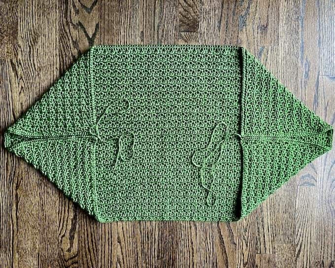 Green textured crochet shrug laid flat with corners folded in to sides to show arm seams