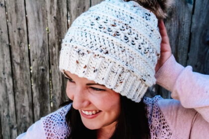 dark haired woman wearing cream and tweed crochet hat with faux fur pom