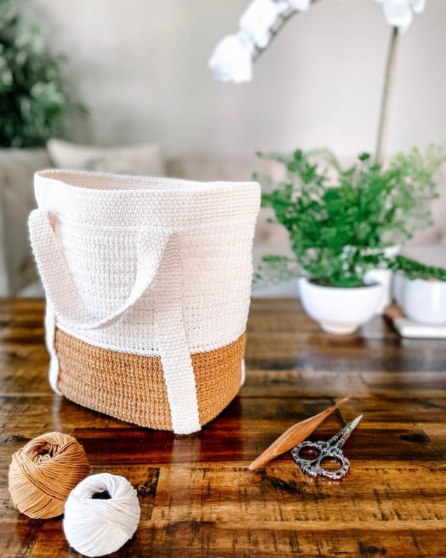Mirabeau crochet tote bag in cream and mustard, sitting upright on a coffee table with yarn and hook nearby