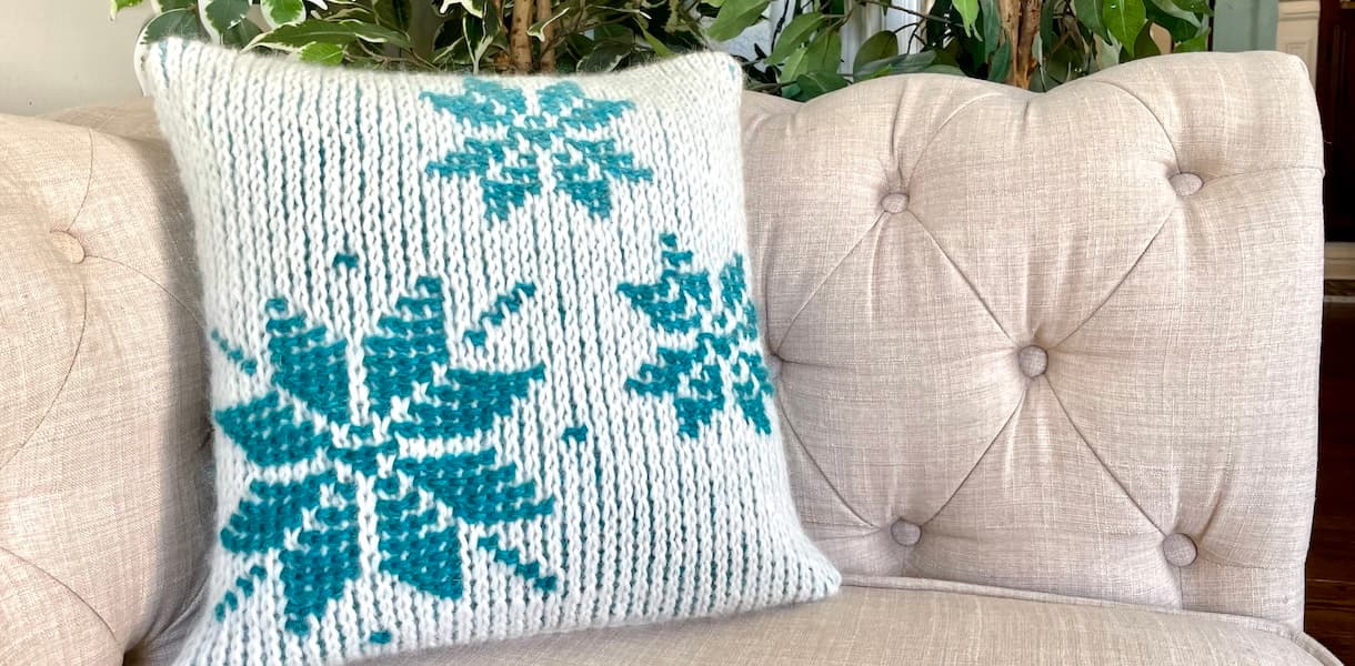 Tunisian Crochet removable cushion cover in cream with blue snowflake motif on cream sofa