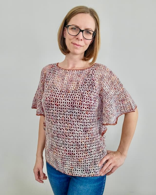 Blonde woman wearing neutral brown lacy crochet top with flowing sleeves and darker brown border