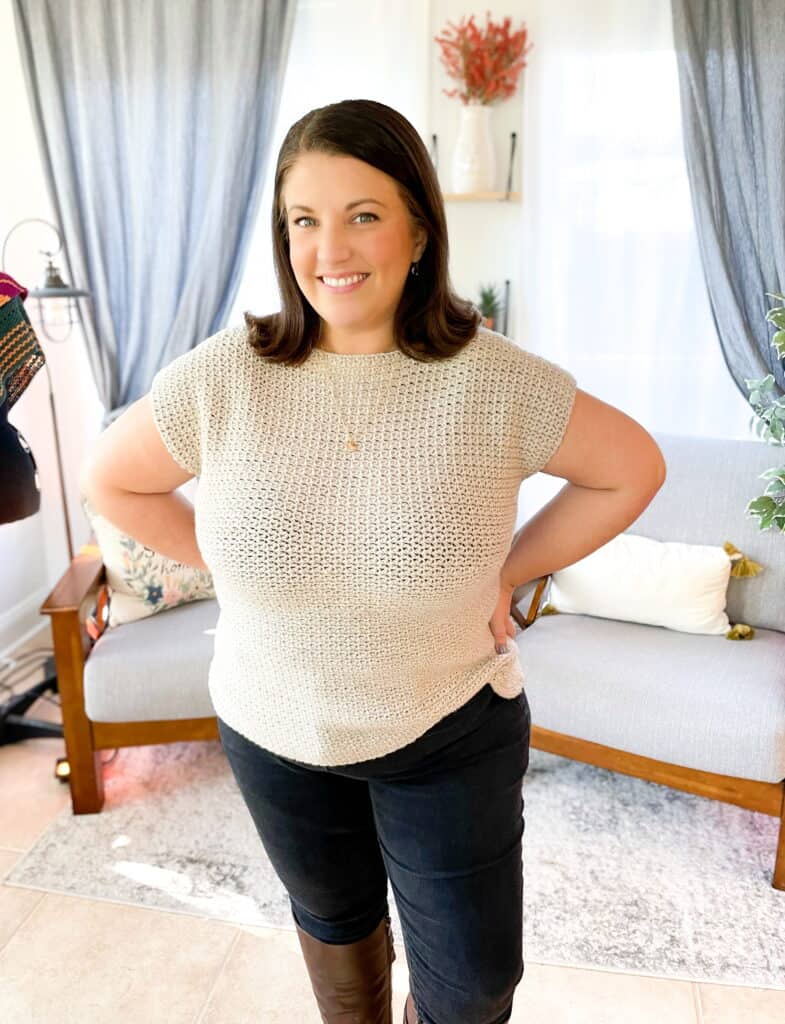 Knitted beige top and black jeans woman standing indoors.